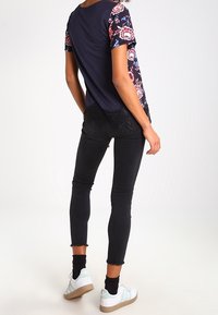 Tmavě modré květované tričko s krátkými rukávy, krajkový lem na okraji, doplněné černými úzkými džíny a bílými teniskami s světle hnědými podrážkami.