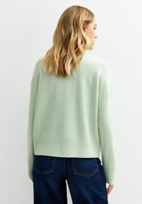 Miętowy sweter o luźnym kroju, z prążkowanym dołem i mankietami, wykonany z miękkiego materiału, pokazany z tyłu, zestawiony z ciemnymi dżinsami.