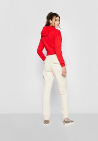 Red cropped hoodie with a hood, paired with white cargo pants featuring side pockets and elastic cuffs. Black and white checkered slip-on shoes.