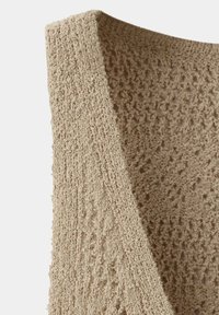 Gros plan d’un tissu tricoté beige avec un motif texturé en boucles montrant un tricot élaboré avec de petits trous partout.