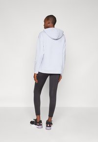 Felpa blu chiaro con cappuccio, abbinata a leggings neri e scarpe sportive nere. Tessuto morbido, vestibilità rilassata e polsini a coste.