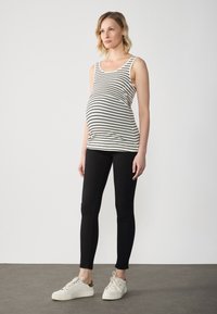 Randig graviditetstopp i krämfärg och svart, åtsittande silhuett, ihopparad med svarta leggings och vita sneakers.