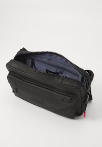 Borsa a spalla in tessuto nero con chiusura a zip, dotata di una tasca frontale e numerosi scomparti interni, inclusa una sezione con zip.