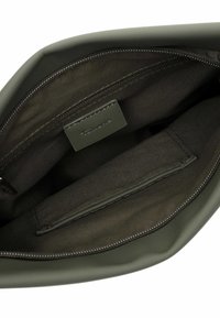 Interno di una borsa verde oliva con finitura liscia e opaca. Presenta una tasca con cerniera e un'etichetta cucita con il nome del marchio.