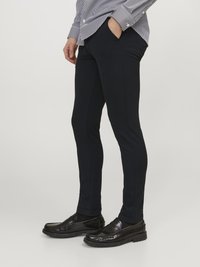 Marineblaue Slim-Fit-Hosen aus Stretchstoff mit Taschendetails, kombiniert mit schwarzen Loafers und einem gestreiften Hemd mit Knöpfen.