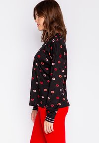 Svart långärmad topp med varierat läpptryck i röda och rosa nyanser. Har en avslappnad passform och randiga ribbade muddar. Matchas med röda byxor.