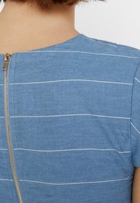 Blue chambray dress with white horizontal stripes, featuring a visible gold zipper at the back and a round neckline. Smooth texture.