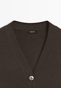 Cardigan marron en maille douce avec un col en V, doté d'une fermeture à un bouton doré unique et de bords côtelés au niveau de l'encolure et de l'avant.