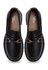 Black leather loafers with a chunky sole, featuring a gold-tone hardware detail and smooth texture. Rounded shape with minimalistic design.