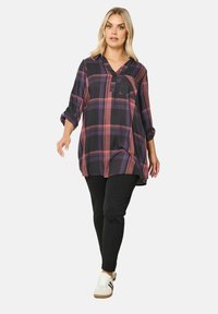 Camicia a maniche lunghe, con colletto, a quadri nelle tonalità blu, rosa e viola, con una tasca sul petto e vestibilità ampia, abbinata a pantaloni neri e sneakers bianche.