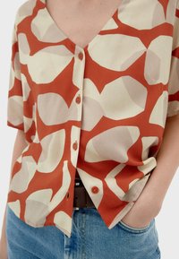 Kurzärmliges Hemd in Rost und Creme mit abstraktem geometrischen Muster, aus leichtem Stoff gefertigt, mit V-Ausschnitt und Knopfleiste.