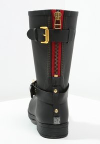 Black rubber boot featuring a red zipper, gold hardware, and a buckle accent. Textured surface with a reinforced heel and smooth finish.