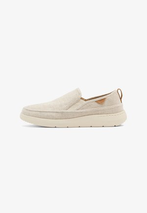 Zapato beige sin cordones con parte superior de tela, suela acolchada, paneles elásticos en los lados y una pestaña marrón para tirar en el talón.