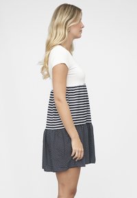 Robe à manches courtes avec un haut blanc et un corsage à rayures bleu marine. Jupe évasée avec un motif à pois, textures et couleurs contrastées.