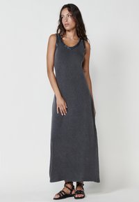 Vestido maxi de tela gris con textura acanalada, diseño sin mangas, escote en V, tirantes adornados, combinado con sandalias negras de tiras.