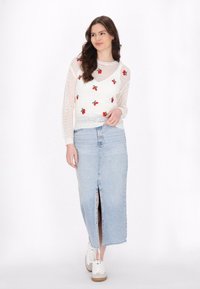 Witte gebreide trui met rode kersenborduursel, gecombineerd met een lichtblauwe denim rok met een voorkant split. Witte sneakers maken de look compleet.