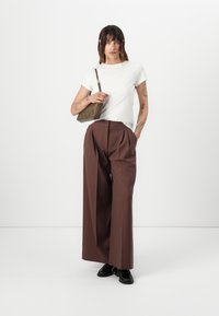 White short-sleeve t-shirt paired with wide brown trousers. Model carries a small olive green handbag with a textured finish. Black shoes.