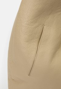 Cream leather handbag with a textured surface, featuring a side zip pocket and smooth stitching accents. Rounded shape, minimalist design.