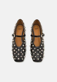 Zapatos Mary Jane de cuero negro con un diseño plano, punteras cuadradas y tachuelas plateadas en la parte superior. Correa con hebilla en el empeine.