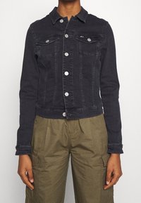 Dark denim cropped jacket with a collar, silver buttons, and two chest pockets. Worn over olive green cargo pants, featuring a smooth texture.