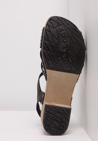 Zwarte sandaal met een gestructureerde rubberen zool, houten tussenzool, uitgesneden ontwerp en metalen accenten langs de bandjes.