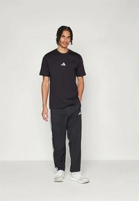 Musta urheilu t-paita, jossa valkoinen Adidas-logo; yhdistetty mustiin housuihin, joissa on valkoiset sivuraitat ja logo. Molemmat on valmistettu pehmeästä kankaasta.