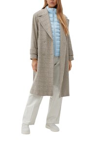 Dvouřadový šedý kabát s kostkovaným vzorem houndstooth, pod kterým je lehká modrá péřová bunda, v kombinaci s krémovými kalhotami a bílými teniskami.