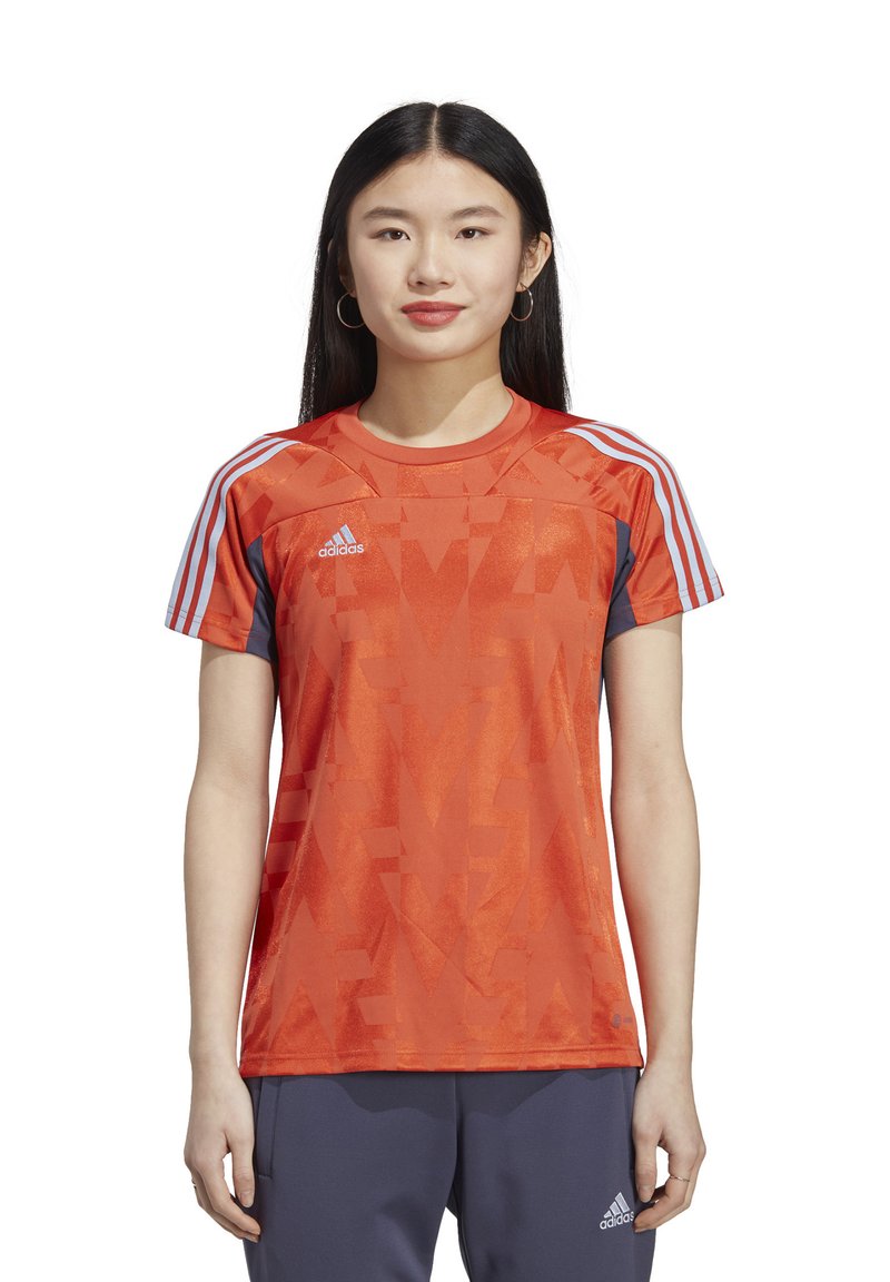 T-shirt de sport rouge avec un motif abstrait, manches courtes, accents bleus, et trois bandes blanches sur les épaules. Logo Adidas sur la poitrine.