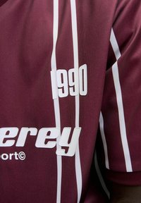 Maroon fabric with vertical white stripes, displaying white raised text "1990" and partial brand name "erey" on the front.