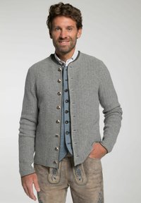 Grauer gerippter Cardigan mit Rundhalsausschnitt, ausgestattet mit metallischen Knöpfen und einem kontrastierenden Innenfutter. Tragen über einem blauen Hemd mit Knöpfen.