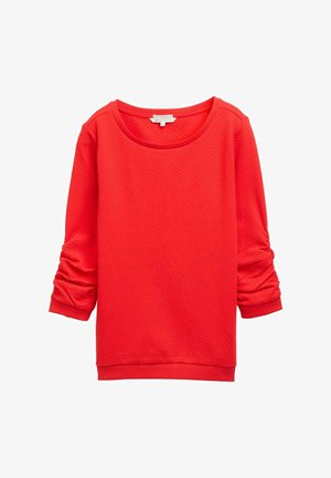 Sarkana sporta jakas ar noapaļotu kakla izgriezumu, garām piedurknēm ar salocījuma detalēm un teksturētu auduma rakstu. Ribota aproces un apakšmala.