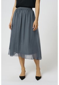 Mörkgrå, ankellång kjol av genomskinligt tyg med elastisk midja och mjuk struktur, draperar elegant. Svarta spetsiga klackar synliga.