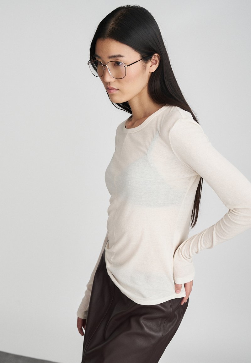 Top ligero de manga larga color crema con escote redondo, textura suave y silueta ajustada, combinado con pantalones de cuero marrón oscuro.