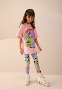 Rosa Baumwoll-T-Shirt mit bunten Cartoon-Grafiken, kombiniert mit gemusterten Leggings in Blau- und Grüntönen, die niedliche Charakterdesigns zeigen.