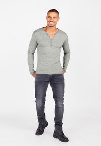 Graues Langarm-Henley-Shirt mit knöpfbarem Ausschnitt, kombiniert mit dunklen Jeans und schwarzen Schnürstiefeln vor einem neutralen Hintergrund.