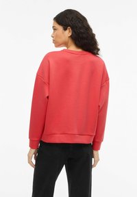 Sudadera roja de corte holgado, con puños acanalados y cuello redondeado. Textura suave y color sólido, combinada con pantalones negros.