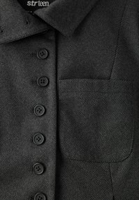 Manteau en laine gris foncé avec six boutons noirs sur le devant et une grande poche plaquée sur le côté droit.