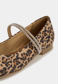 Chaussure plate imprimé léopard avec doubles fines brides en strass et petit talon en bois sur fond clair.