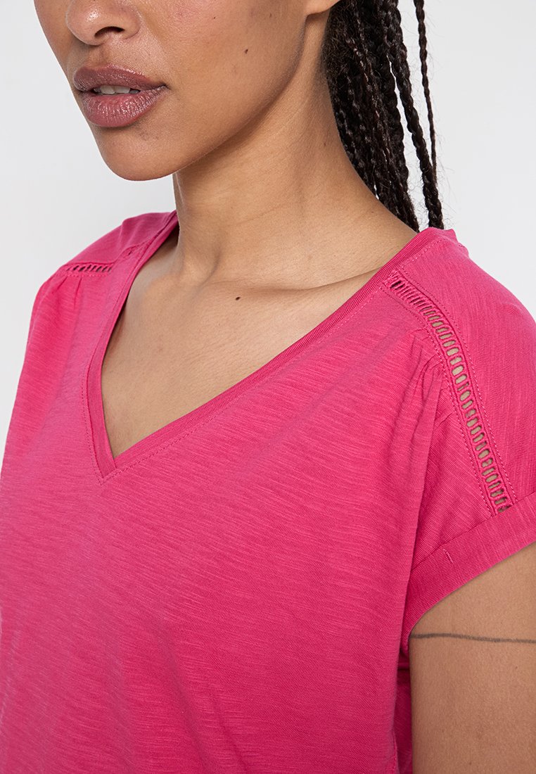 Rosa V-Ausschnitt T-Shirt aus strukturiertem Stoff, mit kurzen Ärmeln und dekorativen Ausschnitten in der Nähe der Schultern.