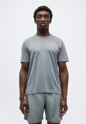 Άνδρας που στέκεται με το πρόσωπο προς τα εμπρός, φορώντας γκρι αθλητική μπλούζα Nike και αντίστοιχα σορτς, σε απλό λευκό φόντο.