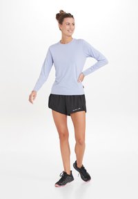 Lys lilla langærmet træningsskjorte parret med sorte shorts. Skjorten har en rund halsudskæring og er lavet af et blødt materiale.