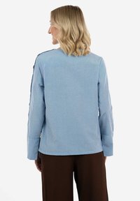 Camicia a maniche lunghe a righe blu e bianche, vestibilità rilassata con spacchi laterali, con dettagli di bottoni sulle spalle e scollatura rotonda.