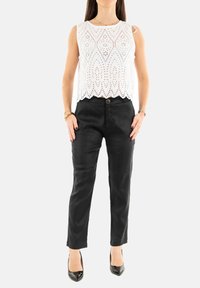 Top blanco sin mangas con detalles de ojales y dobladillo con ondas, combinado con pantalones negros de tiro alto y tacones negros de punta.