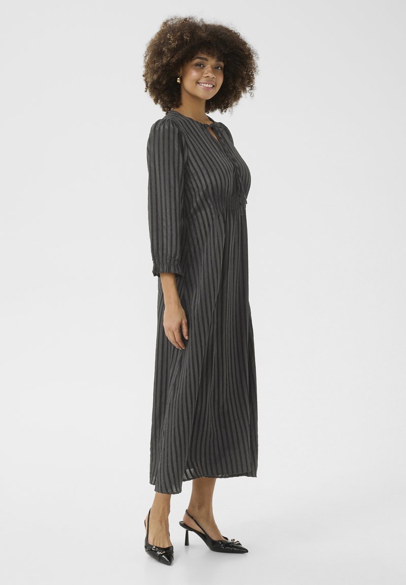 Mustroone ja halli triibuline pikk kleit neljandiku varrukatega, millel on avatud kaelaehe ja smockitud vöökoht. Seljas mustad kontsaga mule'ide kingad.