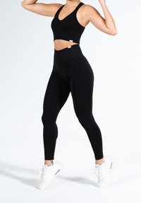 Czarny prążkowany krótki top sportowy i legginsy z wysokim stanem, charakteryzujące się obcisłym dopasowaniem i gładką fakturą, zestawione z białymi tenisówkami sportowymi.