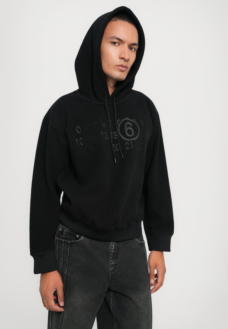 Schwarzer Fleece-Hoodie mit einer großen Kapuze, der hervorgehobene Zahlen und ein kreisförmiges Design auf der Brust zeigt. Weicher Stoff und gerippte Bündchen.