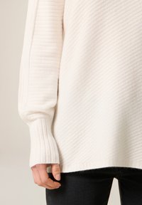 Biały prążkowany sweter z teksturowanym splotem, z długimi rękawami i luźnym krojem, połączony z ciemnymi dopasowanymi dżinsami.