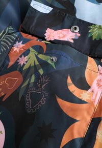Värvikas, mustriline kangas, millel on lille- ja käemotiivid sinise, oranži, roosa ja rohelise toonides. Sisaldab trukknappi ja õmmeldud detaile.