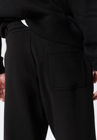 Pantalon de survêtement noir avec une poche carrée à l'arrière, fabriqué en tissu doux avec une texture lisse et une taille élastique pour plus de confort.
