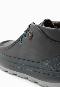 Scarpa nera in pelle con dettagli cuciti, lacci blu e superficie testurizzata. Suola in gomma grigia con un accentuato design sottile.